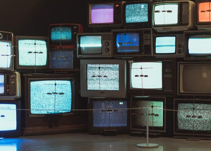 Photo of multiple vintage televisions stacked on top of each other, showing static on their screens.